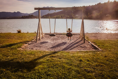 Rear view of girl swinging against lake during sunset