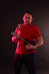 Portrait of young man playing guitar against black background