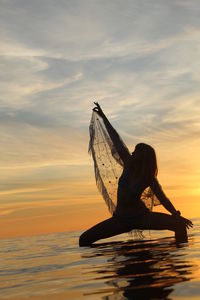 Silhouette woman by sea against sky during sunset