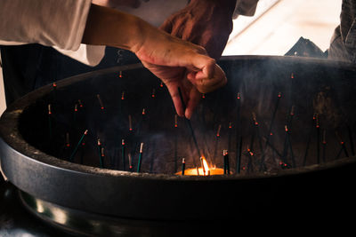 Hand of person igniting incense from flame at temple