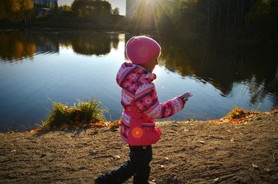 Rear view of girl standing in front of lake on sunny day