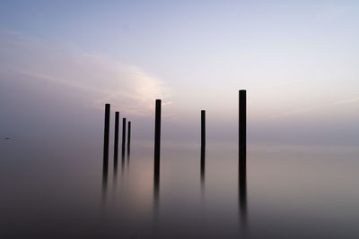 Wooden posts in water against sky during sunset