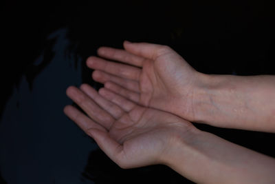 Close-up of hands touching hand over black background