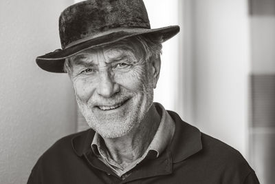 Portrait of smiling senior man wearing hat while standing against wall