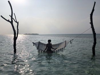 Woman standing by hammock in seashore against sky