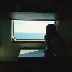 Side view of woman looking through window on tne sea