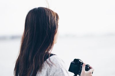 Rear view of woman holding camera at beach