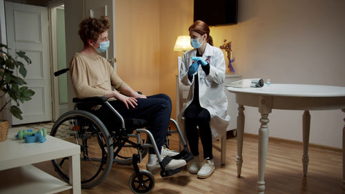 Doctor wearing mask examining patient sitting on wheelchair