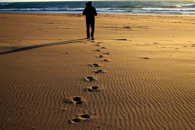 Rear view of man walking at sandy beach during sunset