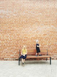 Siblings on bench against brick wall