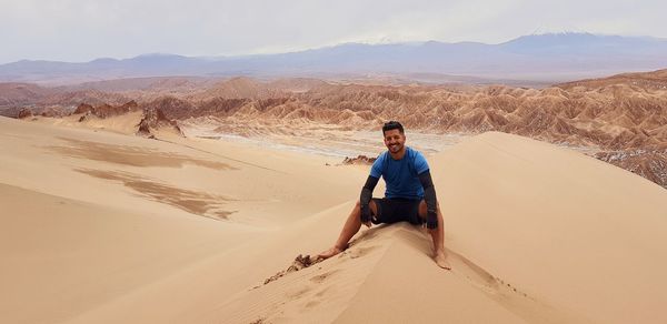 Man sitting on sand dune against sky