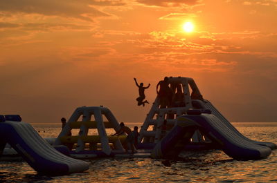 People on jungle gym on sea against sky during sunset