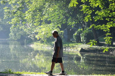 Full length of senior man walking by lake against trees