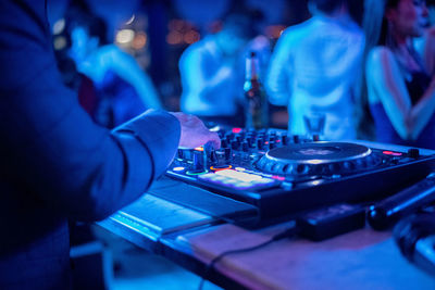 Midsection of man operating sound mixer with people in background in music concert at night