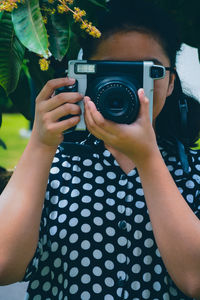 A girl wearing a polkadot dress holding an slr camera obscuring her face 