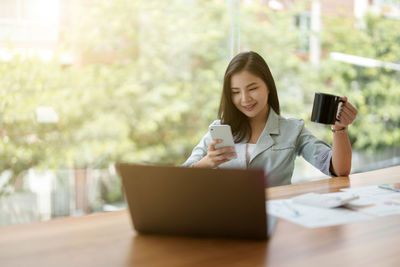 Young woman using mobile phone while sitting on table