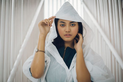 Portrait of young woman wearing raincoat against window
