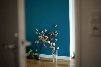 Flowers in vase against blue wall seen through doorway at home