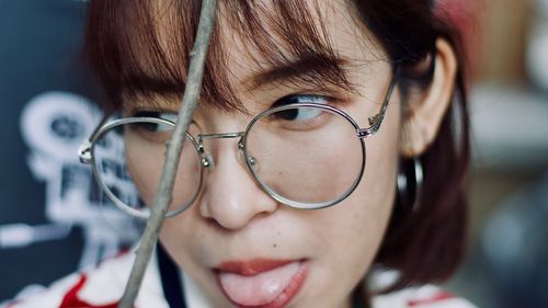 Close-up of thoughtful woman wearing eyeglasses while sticking out tongue