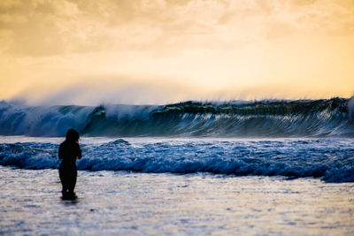 Rear view of woman standing at beach during sunset