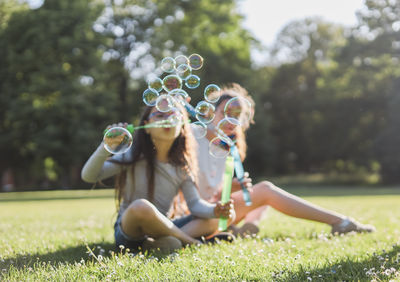 Blurred background two caucasian girls-sisters blowing soap bubbles in the park.