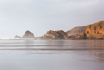 Rock formations on beach against sky