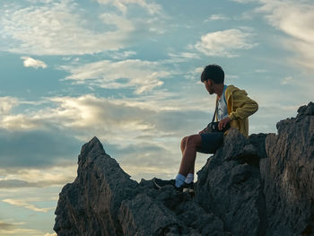Boy sitting on top of rock formation sky views and overlooking