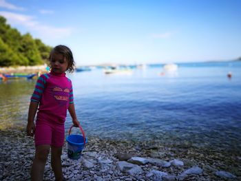 Girl holding bucket while standing at beach against blue sky