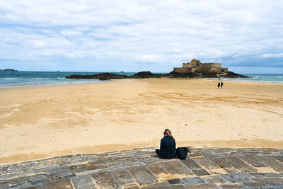 Woman sitting on beach in front of an old castle ruin in the bretagne