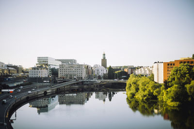 Kungsholmen town hall amidst modern buildings reflected in sea against clear sky