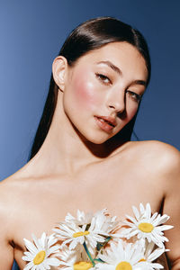 Portrait of young woman with red flower against blue background