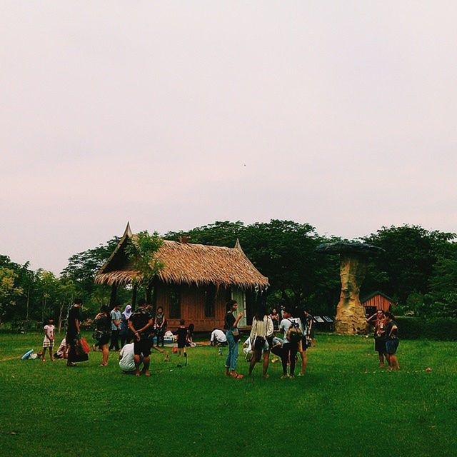 grass, large group of people, men, person, lifestyles, leisure activity, copy space, field, clear sky, green color, tree, relaxation, togetherness, mixed age range, grassy, sitting, landscape, sky, architecture