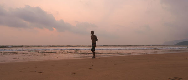 Man standing on beach against sky during sunset