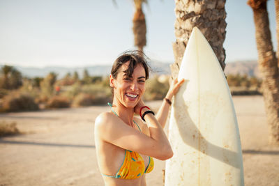 Portrait of smiling woman with surfboard standing at beach