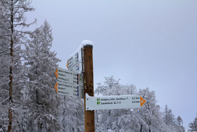 Information sign by trees against sky during winter