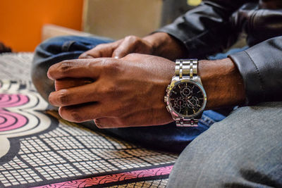 Close-up of man wearing wristwatch on bed at home