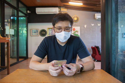 Portrait of young man using phone while sitting on table