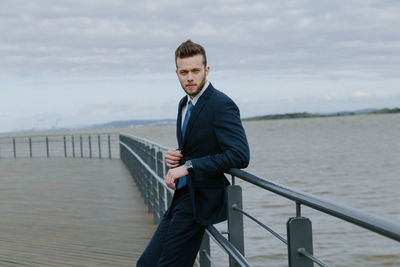 Portrait of handsome man leaning on railing against sea