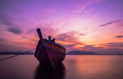 Boat moored in sea against sky during sunset