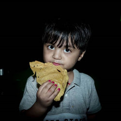 Portrait of boy holding ice cream against black background