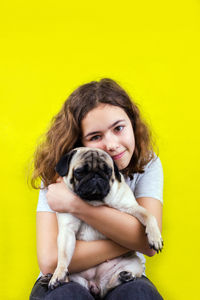 Portrait of teenage girl with dog against yellow background