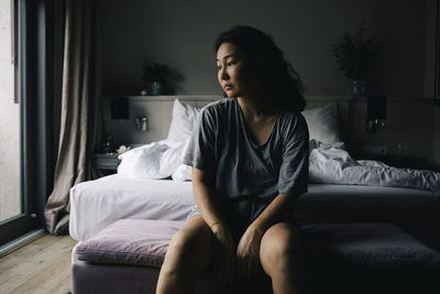 Mentally exhausted woman sitting on bed end bench in bedroom at home