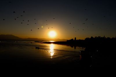 Silhouette birds flying over lake against sky during sunset