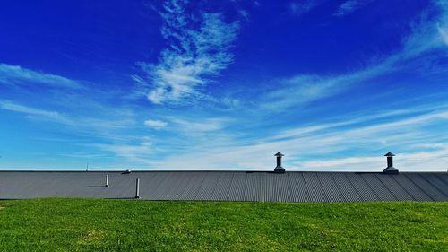 Roof by grassy field against blue sky