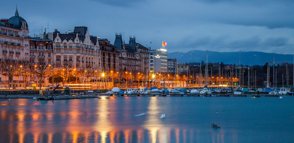 Buildings by lake against sky in city at dusk