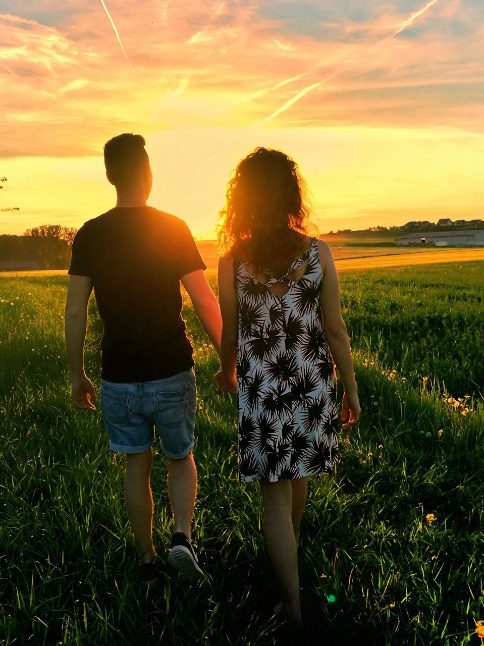 REAR VIEW OF SIBLINGS STANDING ON FIELD AGAINST SKY