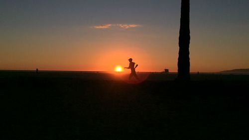 Silhouette man standing on landscape against orange sky