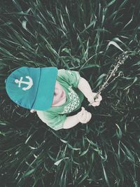 High angle view of boy in green cap holding plant amidst corn field
