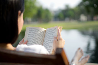 Midsection of man reading book against blurred water