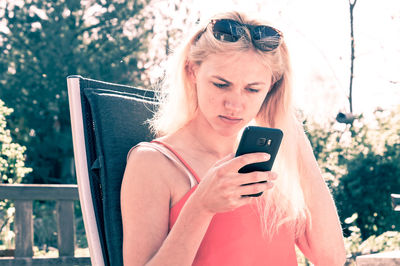 Young woman using mobile phone while sitting on chair